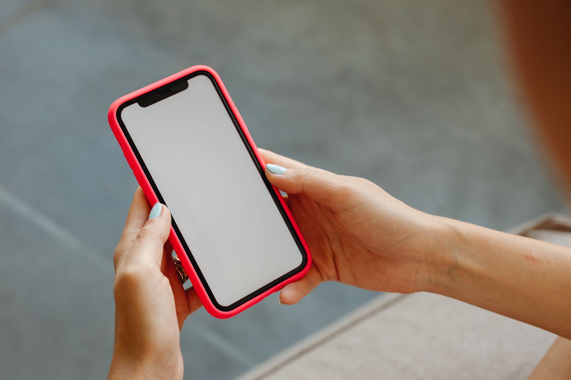 Dłonie trzymają smartfon w czerwonym etui z pustym ekranem