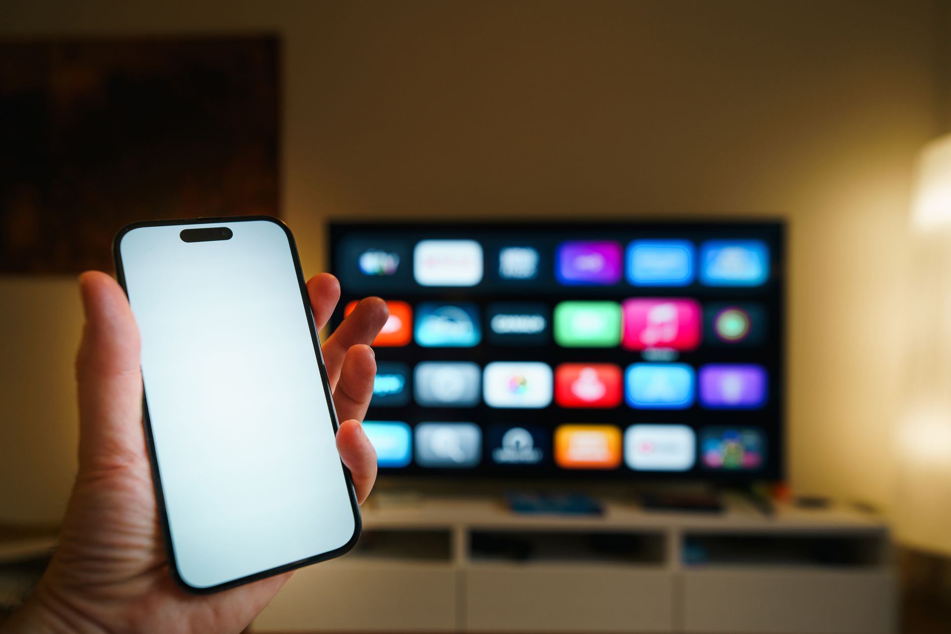 Dłoń trzyma smartfon przed telewizorem z ekranem aplikacji